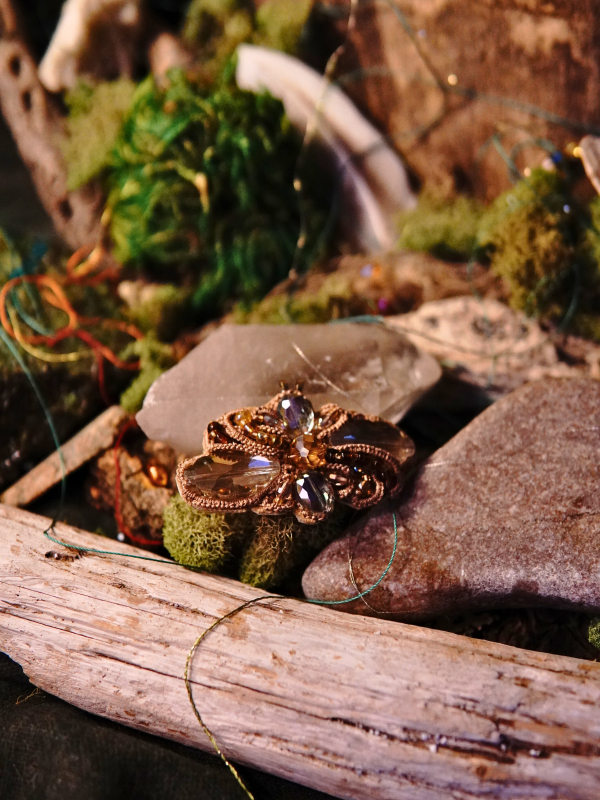 Forestflare tatted lace pin/pendant with warm crystal accents Forest-themed lace pendant resting on driftwood