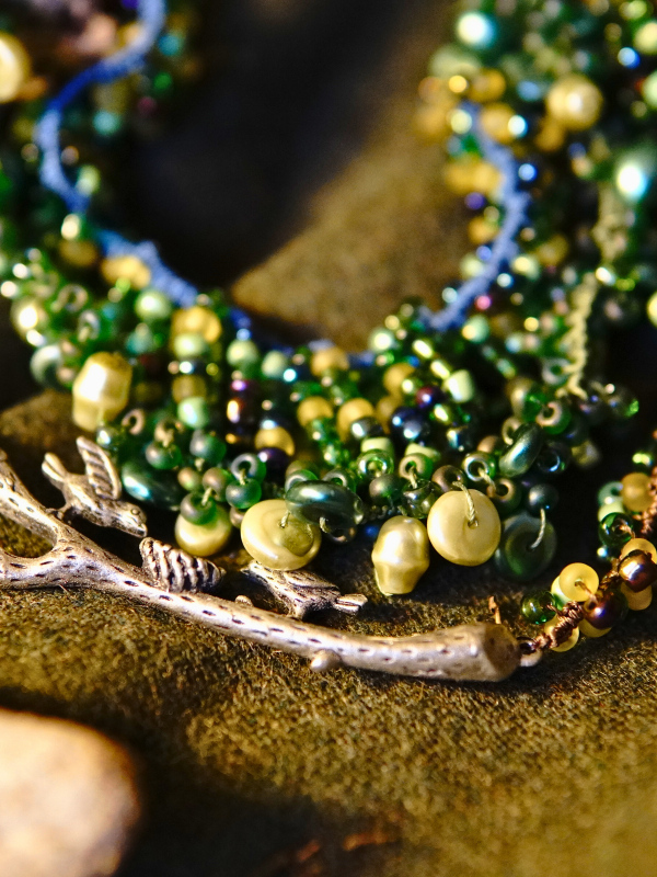 Three-strand tatted woodland necklace in brown, green, and blue hues Close-up of green and brown lace necklace on forest backdrop