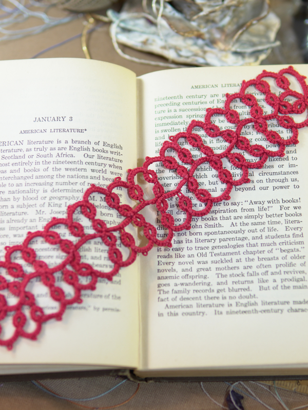 Cranberry Lace Bookmark Deep cranberry tatted lace bookmark resting on the pages of an open book