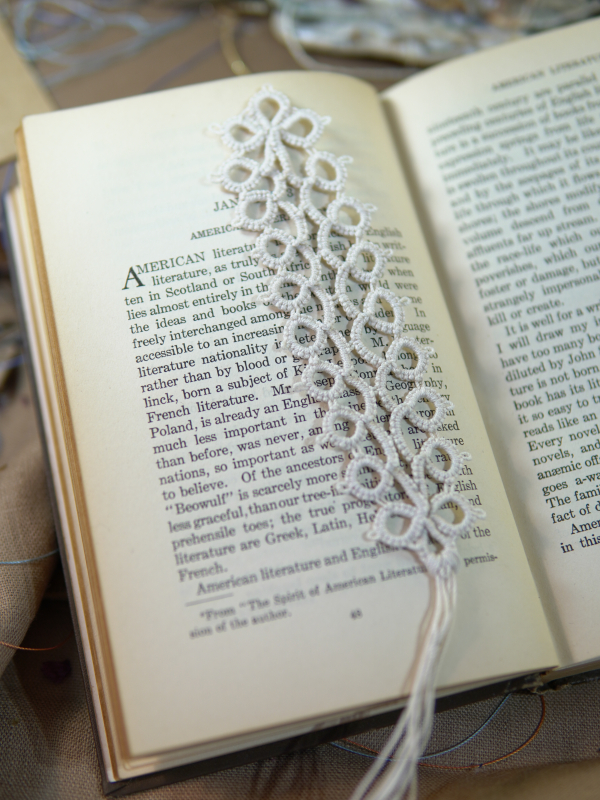 Ivory Whisper Bookmark White tatted lace bookmark with tassel resting on the pages of an open book