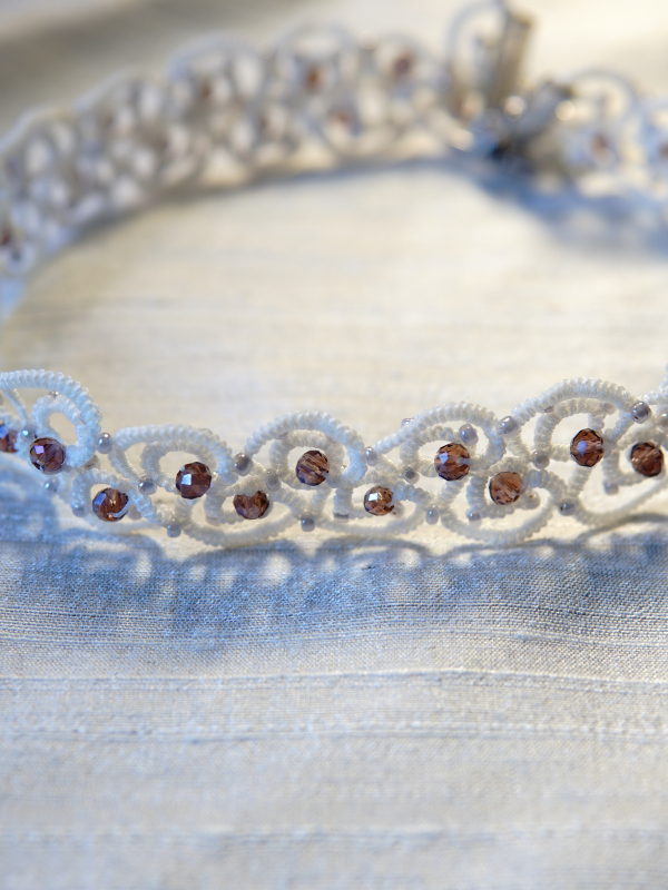 Elarian Bloom Necklace with crystals White tatted necklace with pink crystals displayed on pale fabric.