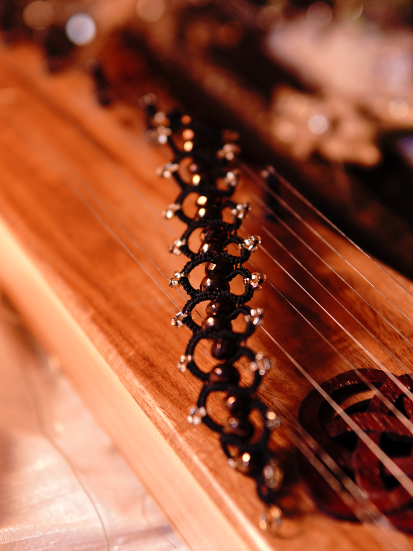 Elven-inspored Emberveil Binding bracelet from Whispers of Aeluin Black tatted bracelet with bronze beads resting on wooden instrument
