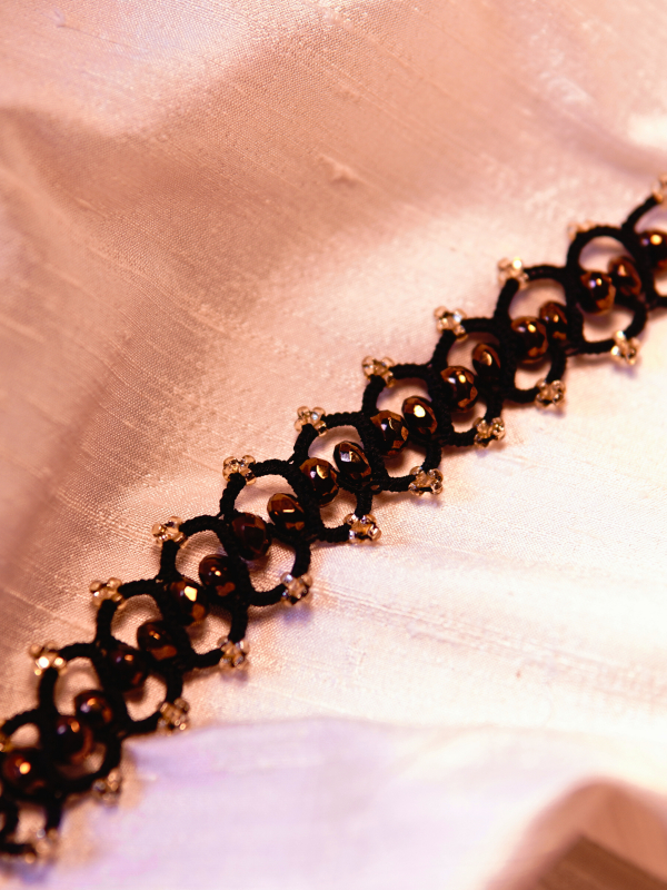 Elven-inspored Emberveil Binding bracelet from Whispers of Aeluin Black tatted bracelet with bronze crystal beads laid flat on white silk fabric