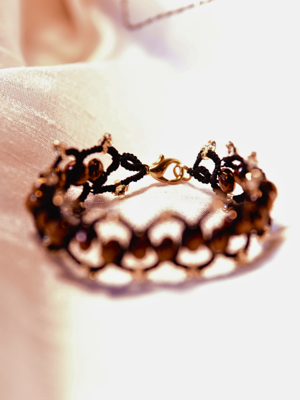Elven-inspored Emberveil Binding bracelet from Whispers of Aeluin Black tatted bracelet with bronze crystal beads laid flat on white silk fabric