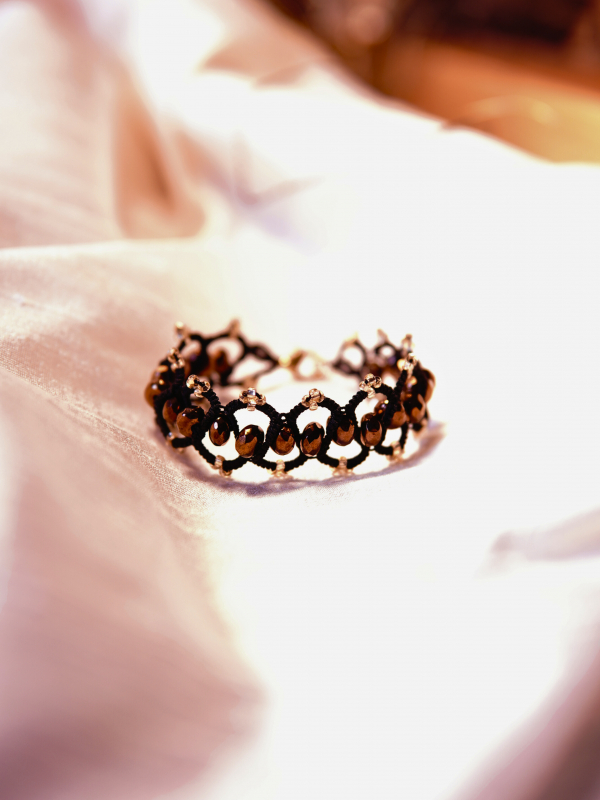 Elven-inspored Emberveil Binding bracelet from Whispers of Aeluin Black tatted bracelet with bronze crystal beads laid flat on white silk fabric