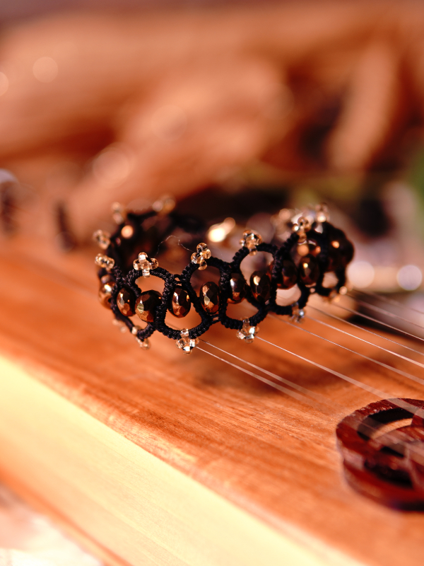 Elven-inspored Emberveil Binding bracelet from Whispers of Aeluin Black tatted bracelet with bronze beads resting on wooden instrument