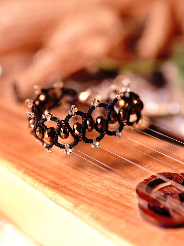 Elven-inspored Emberveil Binding bracelet from Whispers of Aeluin Black tatted bracelet with bronze beads resting on wooden instrument