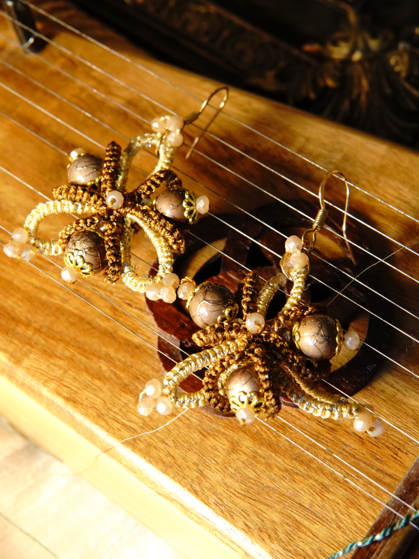 Hearthshade folded-ring tatted lace earrings in warm tones Hearthshade earrings resting on a wooden stringed instrument