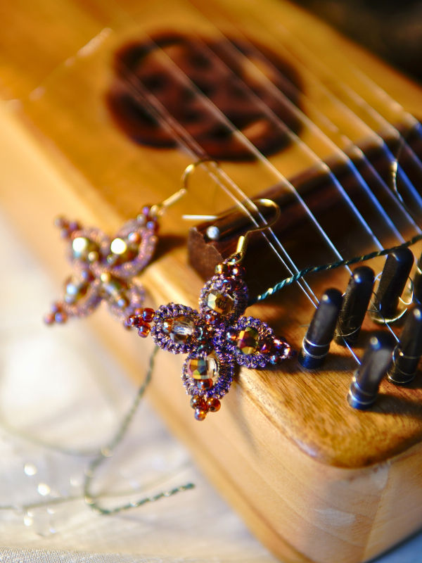 Starweft Blossom tatted lace earrings in pink and crystal Pink lace earrings with crystals shown beside a wooden instrument.