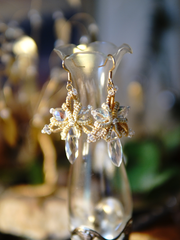 Sunstar golden tatted lace earrings with crystal drops Sunstar earrings hanging on glass vase in warm light