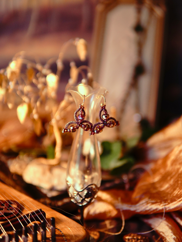 Triune-shaped pink lace earrings glowing in warm golden light.