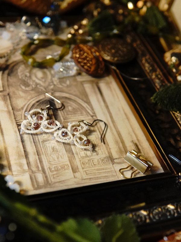 The Elarian Bloom Earrings shimmer with pale rose crystals in white tatted lace. Detailed shot of lace loops and pink crystals.