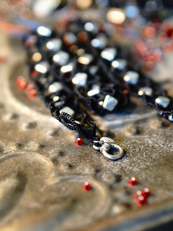 Ironveil Oath—midnight lace and silvered resolve Black tatted necklace with silver beads on metal surface