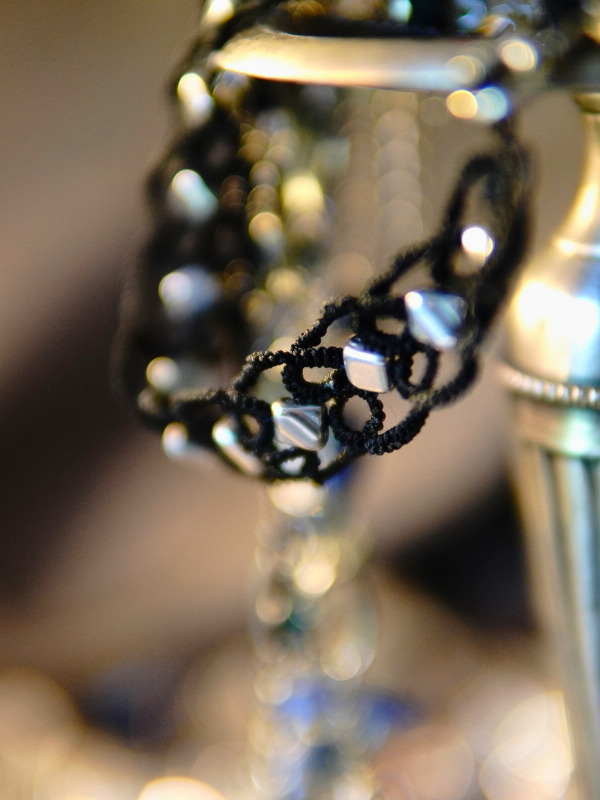 Ironveil Oath—midnight lace and silvered resolve Close-up of black tatted necklace with silver accents on a metal surface.