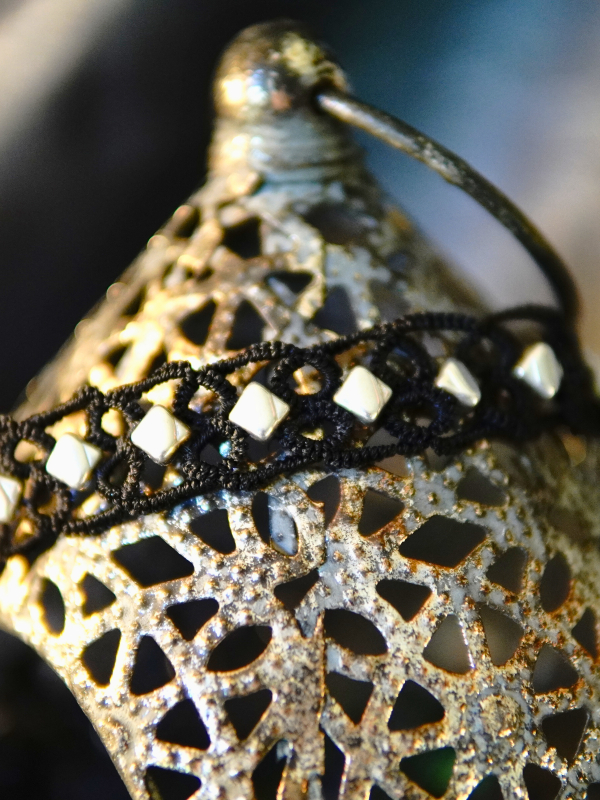 Ironveil Oath—midnight lace and silvered resolve Necklace draped over metal lantern with soft light