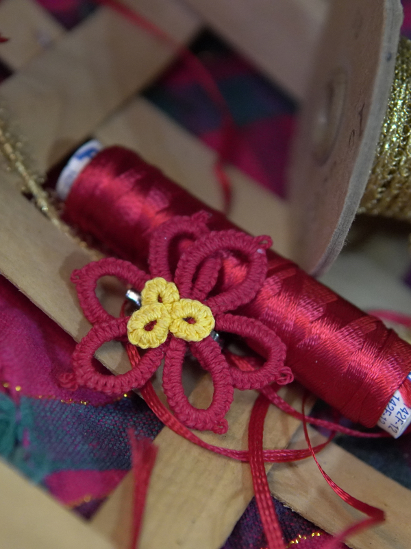 Tatted red and yellow poinsettia pin displayed with festive ribbon