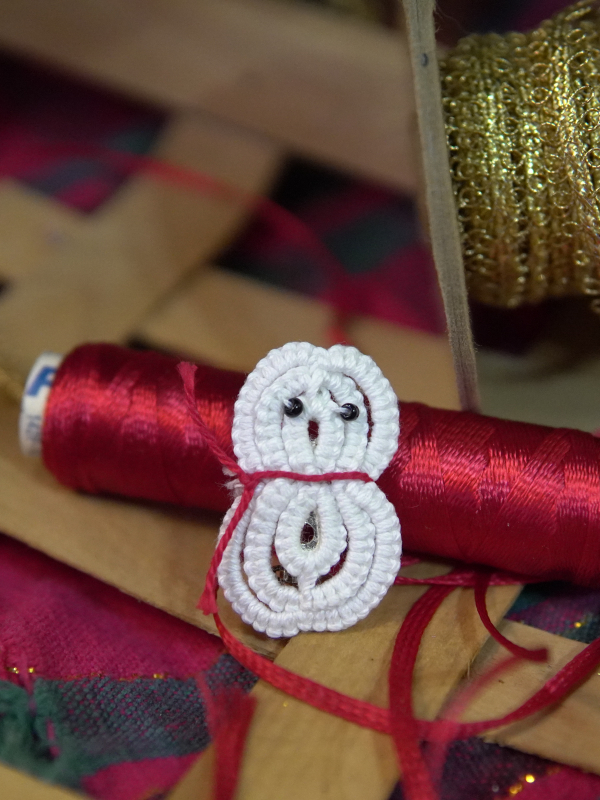 Small white tatted snowman pin resting against red thread spool