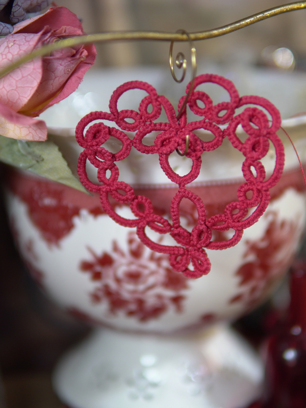 Lace heart ornament in deep red shown against romantic tabletop props.