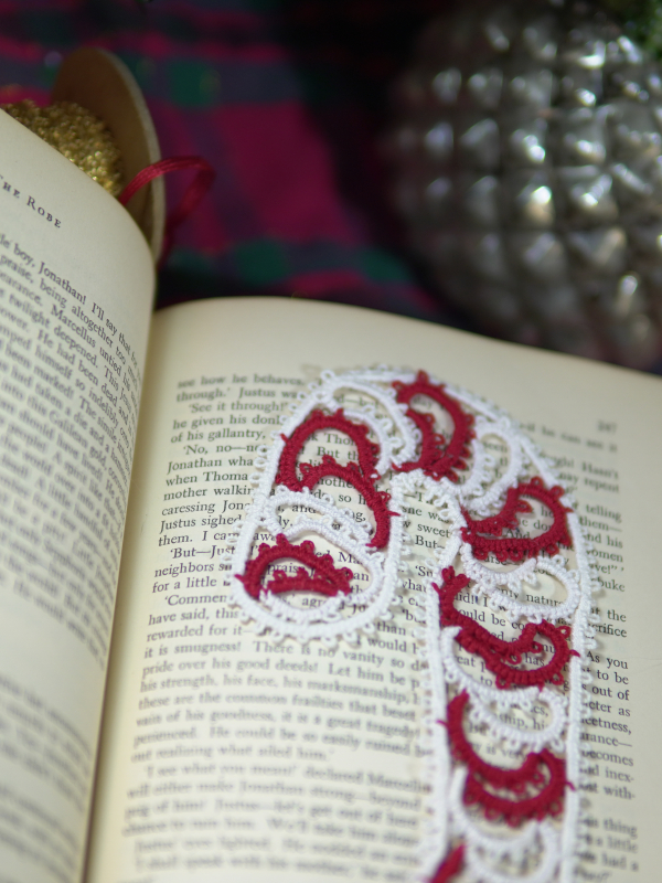 Festive tatted lace candy cane bookmark displayed across vintage book pages in a