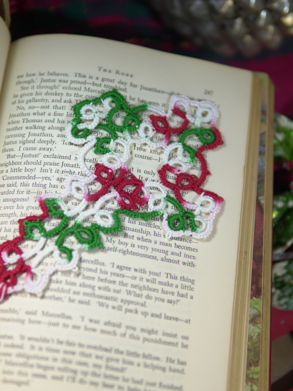 Intricately tatted Christmas cross bookmark set on an open book with holiday déc