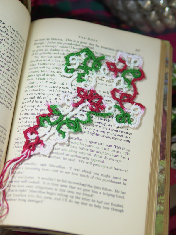 Hand-tatted lace Christmas cross bookmark in red, white, and green resting on th