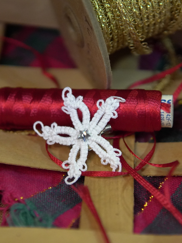 White tatted star pin with crystal center beside gold trim spool