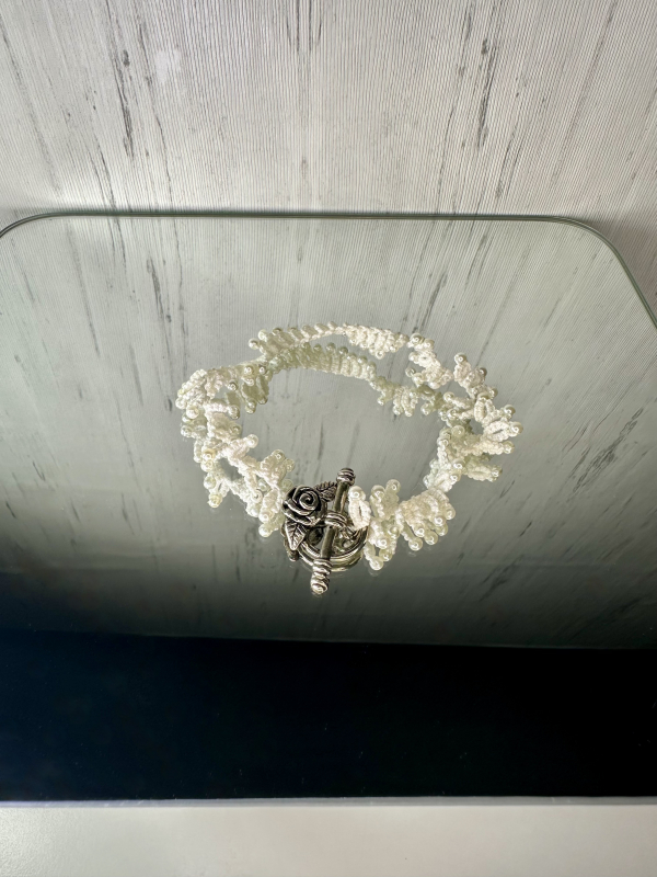 Rose & Ruffle Tatted lace bracelet displayed on a mirror. White tatted lace bracelet displayed on a mirror.