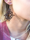 Close-up of handmade brown lace earrings in sunlight.