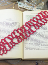 Deep cranberry tatted lace bookmark resting on the pages of an open book