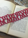Handmade red tatted lace bookmark displayed across open vintage book pages