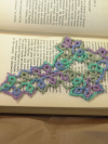 A delicate tatted lace cross bookmark in soft sea-green and lavender tones