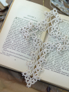 Elegant white tatted lace cross bookmark laid across an open book