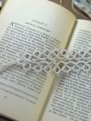 Ivory tatted lace bookmark lying on an open book with soft background props