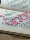 Pink tatted lace Josephine Knot bookmark resting on the pages of an open book