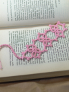 Handmade pink tatted Josephine Knot bookmark displayed on an open vintage book