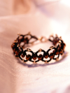 Black tatted bracelet with bronze crystal beads displayed on white silk fabric