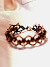 Black tatted bracelet with bronze crystal beads laid flat on white silk fabric