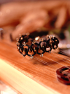 Black tatted bracelet with bronze beads resting on wooden instrument