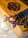 Pink lace earrings with crystals shown beside a wooden instrument.
