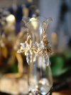 Sunstar earrings hanging on glass vase in warm light