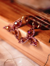 Pink tatted earrings with crystals resting on a wooden instrument.