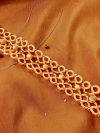 Braceelt made of coral tatted lace and shining glass beads on warm fabric