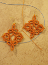 Orange lace earrings laid flat to showcase symmetrical design.