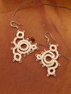 Close-up of handmade tatted lace earrings named Whirlwind against warm fabric.