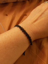 Black tatted bracelet on a wrist against a rustic background.