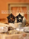 Star-shaped earrings in black thread with warm natural backdrop.