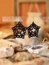Black tatted star drop earrings agains boho backdrop