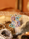Pastel earrings displayed in front of a bohemian background.