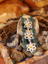 Green and white tatted daisy bracelet draped across natural rock
