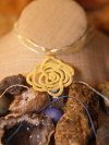 A single spiral lace rose in golden thread lies centered on bohemian background